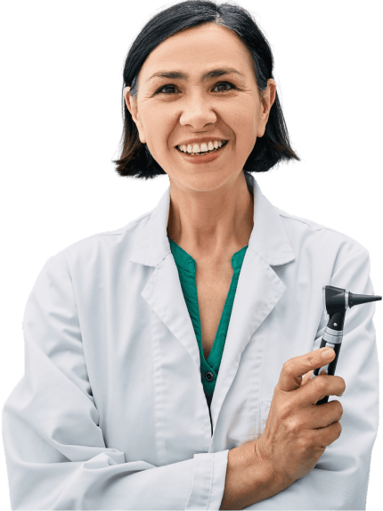 A photo of a dark-haired female audiologist in a white lab coat holding an otoscope with her arms crossed and smiling.